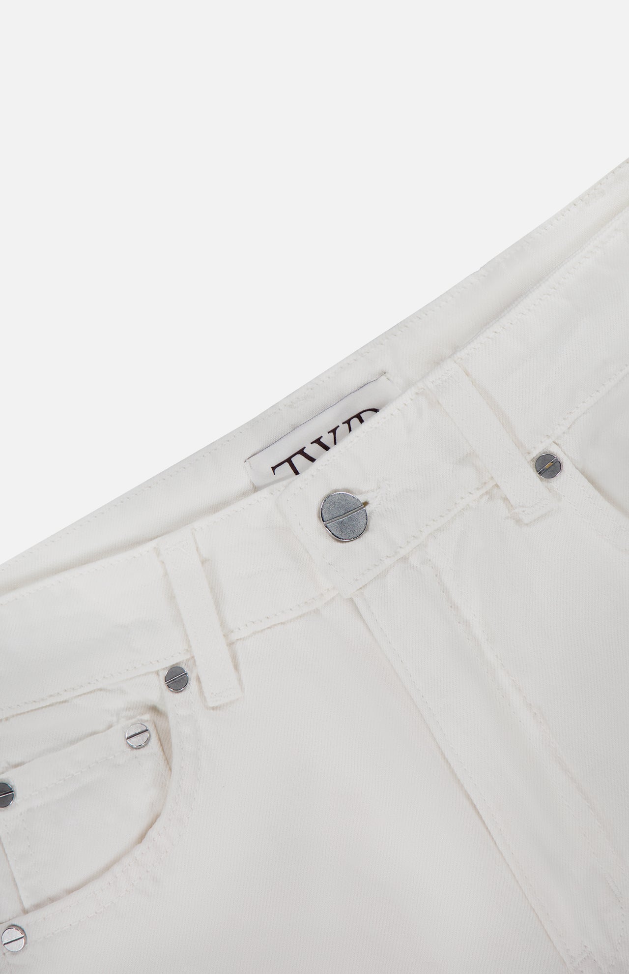 Close-up of the waistband and front pocket of the TWP West 11th St Pant in white linen-cotton denim, showing silver rivets, a button, and the brand’s label inside.