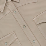 Close-up of the TWP Yellowstone Western Blouse in beige, featuring silver snap buttons, two chest flap pockets, and visible white stitching. A portion of the inner collar label with black text is also visible.