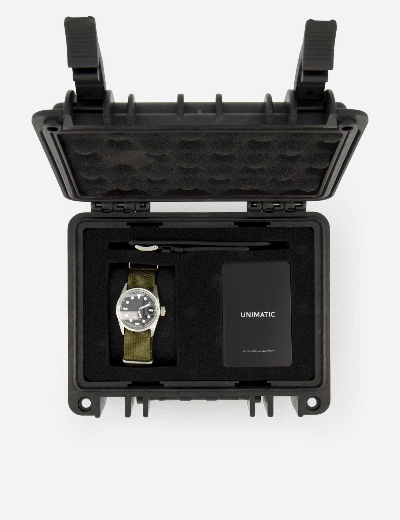 The Unimatic Watch Kit U5S-BL by UNIMATIC includes a diving watch with a green strap, featuring Swiss automatic movement and made in Italy, presented in a black protective case alongside a key and a black UNIMATIC-labeled card, all securely arranged within foam compartments.