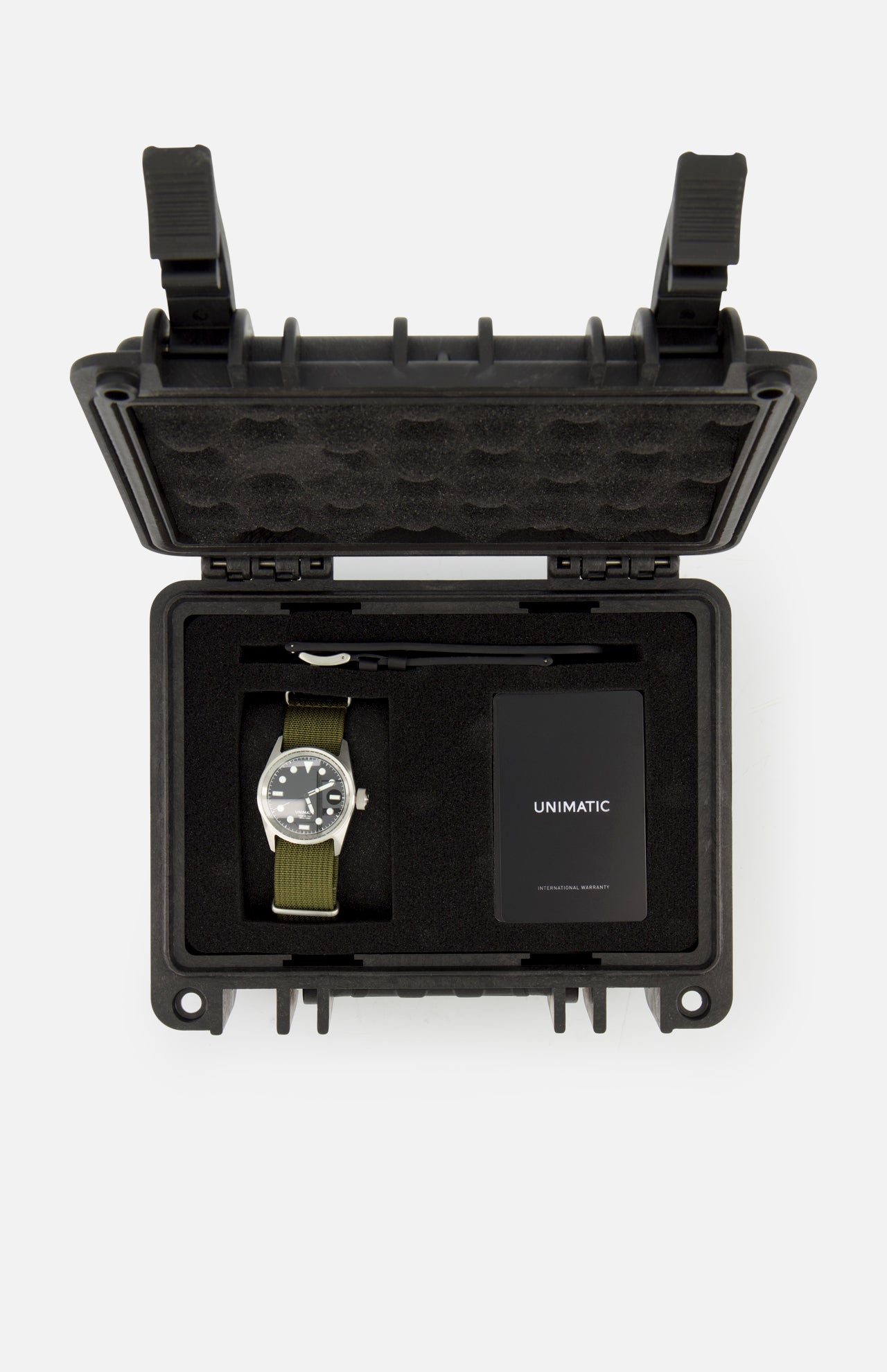 The Unimatic Watch Kit U5S-BL by UNIMATIC includes a diving watch with a green strap, featuring Swiss automatic movement and made in Italy, presented in a black protective case alongside a key and a black UNIMATIC-labeled card, all securely arranged within foam compartments.