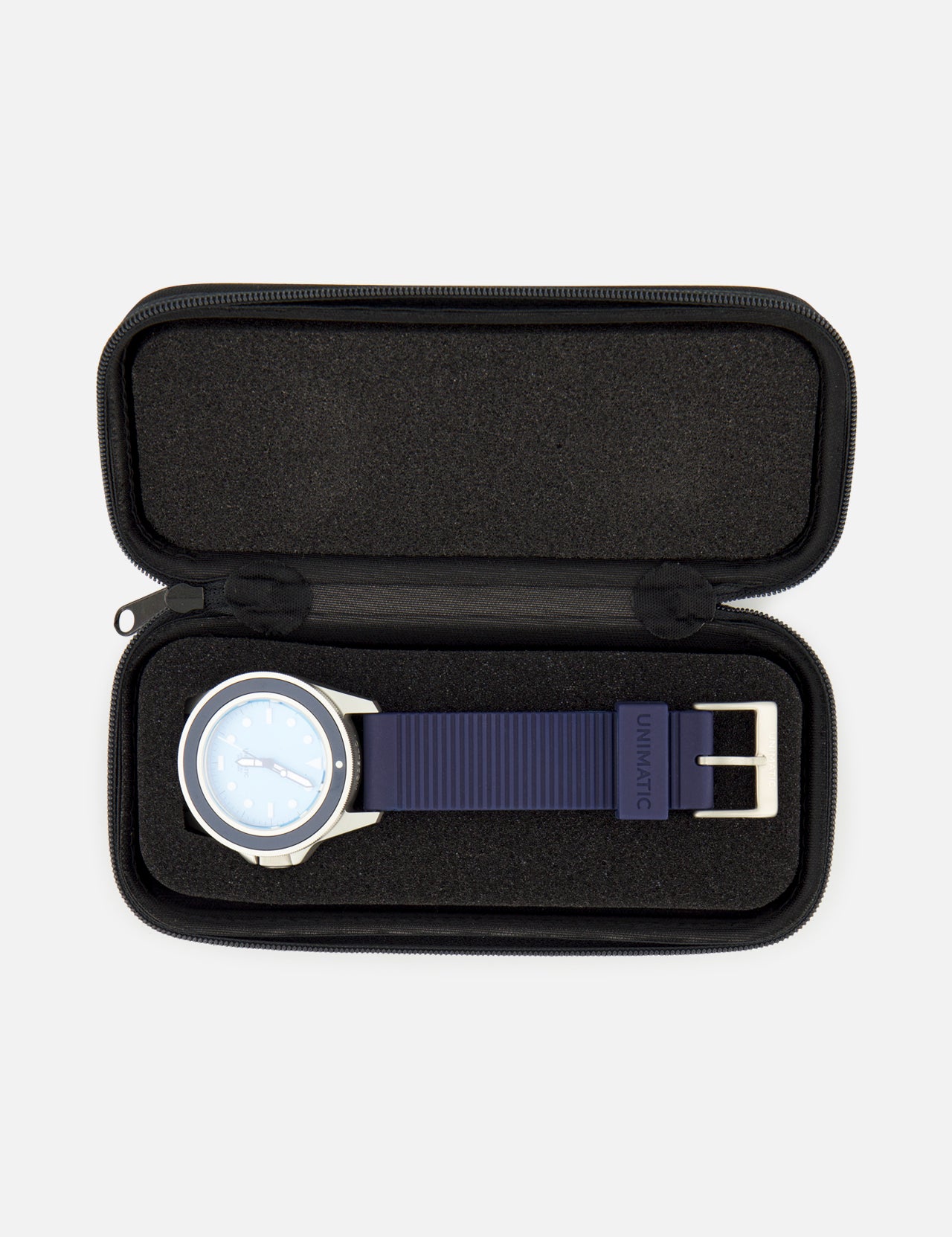 A UNIMATIC UT1-IP Chromatic Trilogy Watch, featuring a blue dial, silver case, and blue strap, is displayed inside an open black zippered case with a foam interior.