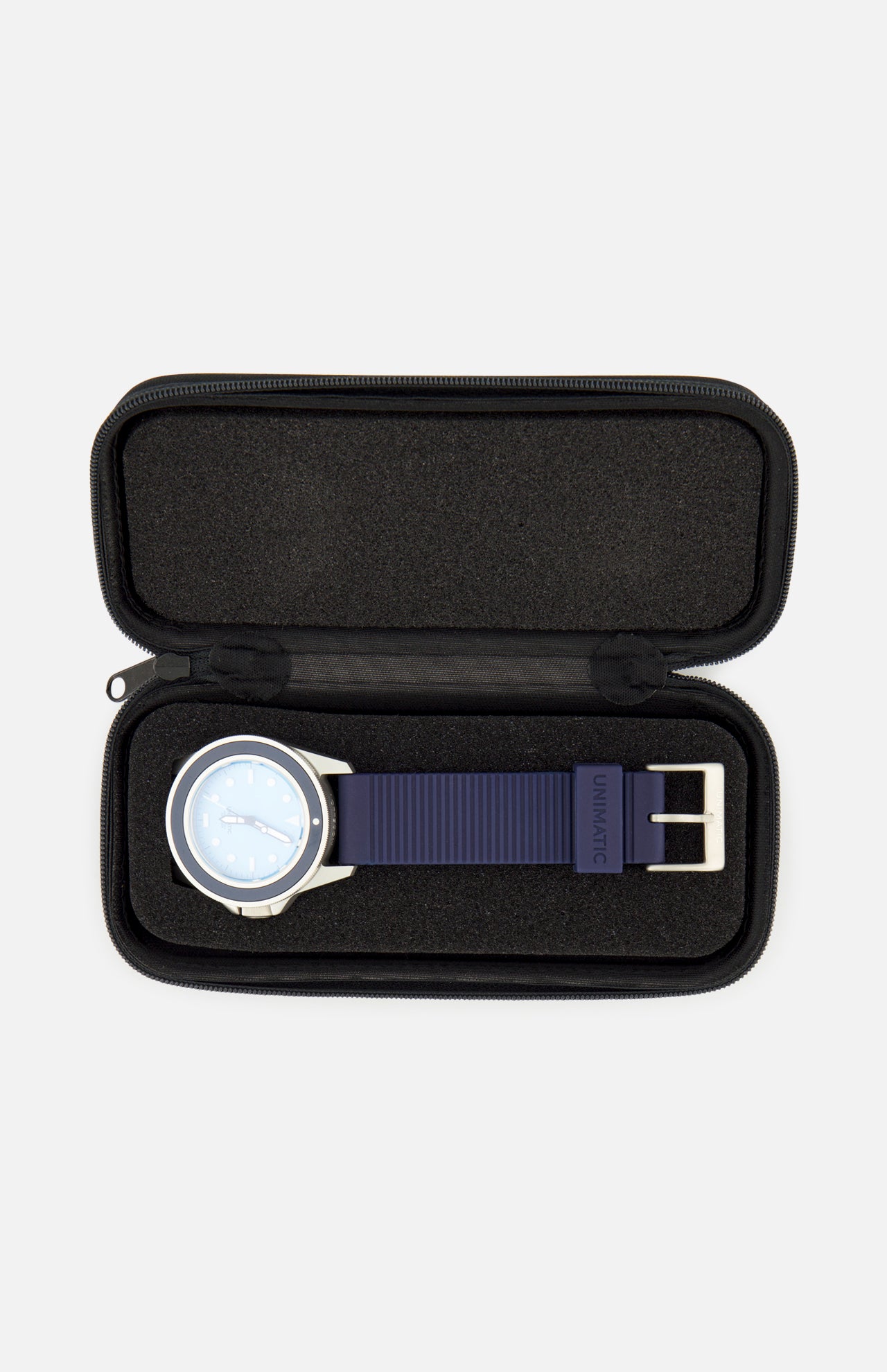 A UNIMATIC UT1-IP Chromatic Trilogy Watch, featuring a blue dial, silver case, and blue strap, is displayed inside an open black zippered case with a foam interior.