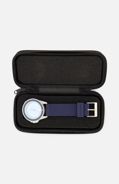 A UNIMATIC UT1-IP Chromatic Trilogy Watch, featuring a blue dial, silver case, and blue strap, is displayed inside an open black zippered case with a foam interior.