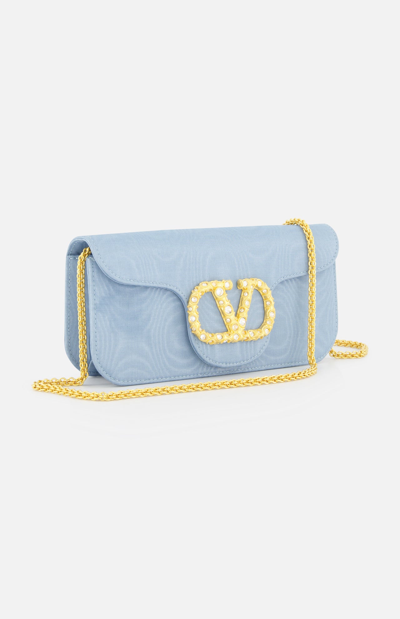 A compact light blue VALENTINO GARAVANI Loco Swarovski Crystal Clutch features a gold chain strap and a crystal-embellished VLogo Signature clasp on the front flap, styled against a plain white background.