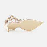 The Rockstud Ankle Strap Heel T.65 by VALENTINO GARAVANI, a beige patent leather pump with gold rockstuds and multiple ankle straps, is shown on its side revealing the sole and pointed toe against a plain white background.