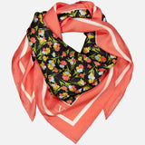 The VALENTINO GARAVANI Shawls Fouland Silk Scarf is a square Italian-made silk scarf with a coral pink border, black center, and colorful floral print in red, yellow, and green, styled in a loose, layered fold.
