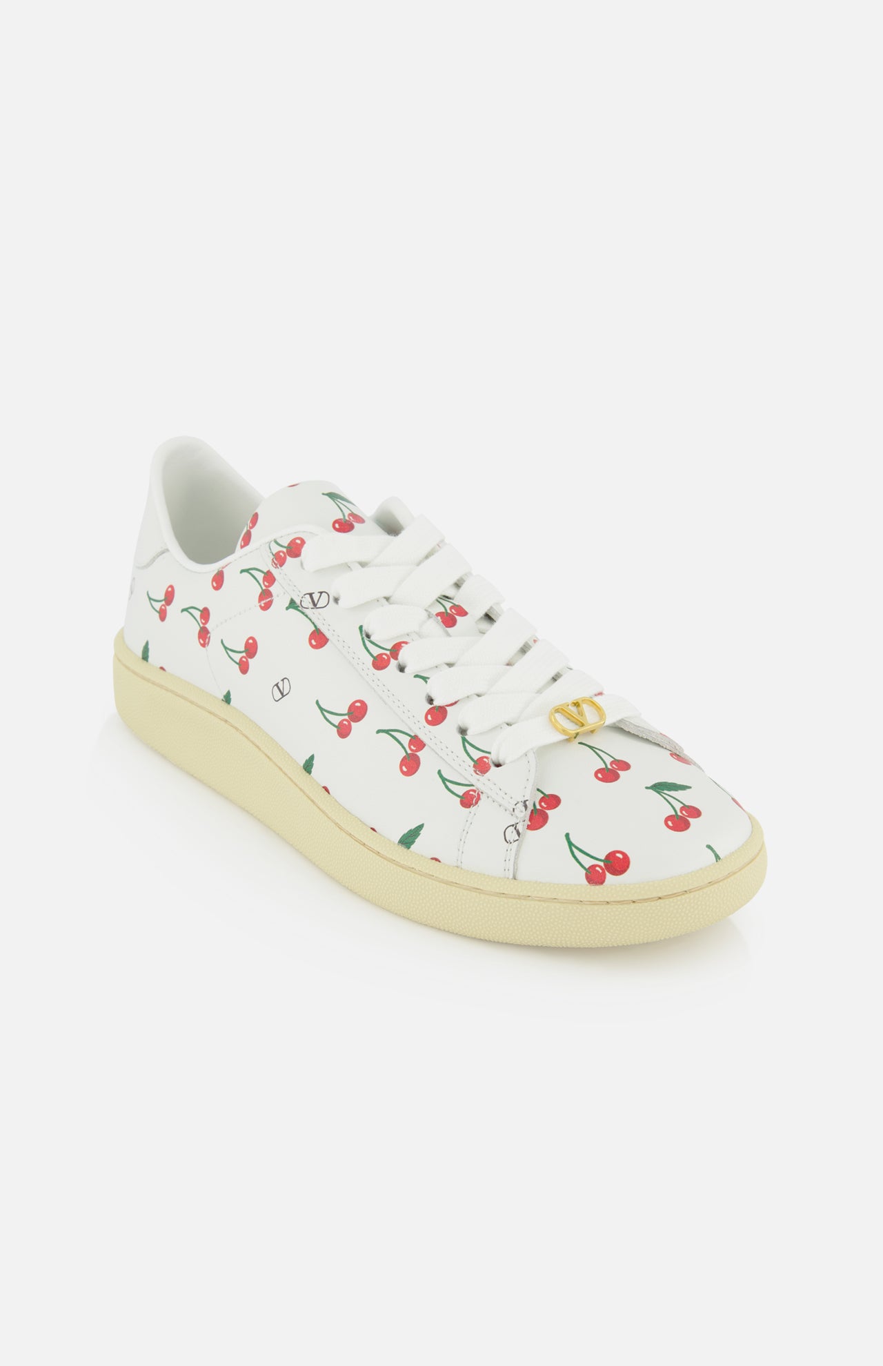 The Valentino Garavani Royco Sneaker by VALENTINO GARAVANI, featuring cherry patterns, white laces, and a light beige sole, is displayed on a plain white background to highlight its playful designer style.