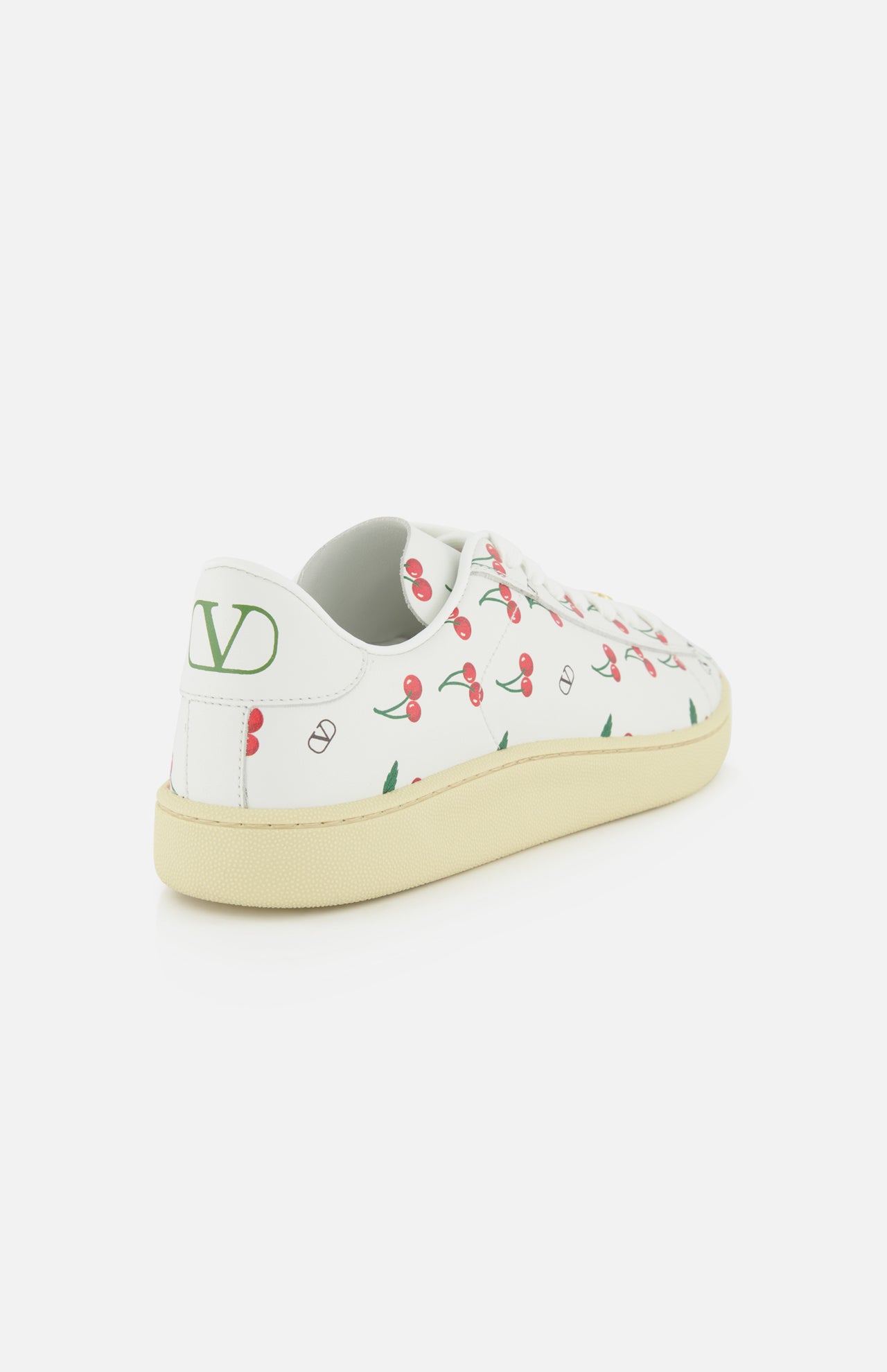 The Valentino Garavani Royco Sneaker by VALENTINO GARAVANI features playful red cherry and green leaf prints, a beige sole, bold green V logo on the heel, and white leather construction, shown against a plain white background.