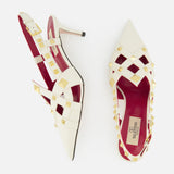 VALENTINO GARAVANI’s Studdy Sling Back Heel T.65 features ivory leather, pointed toes, gold pyramid studs, crisscross ankle straps, red insoles, and slender heels—displayed on a white background.
