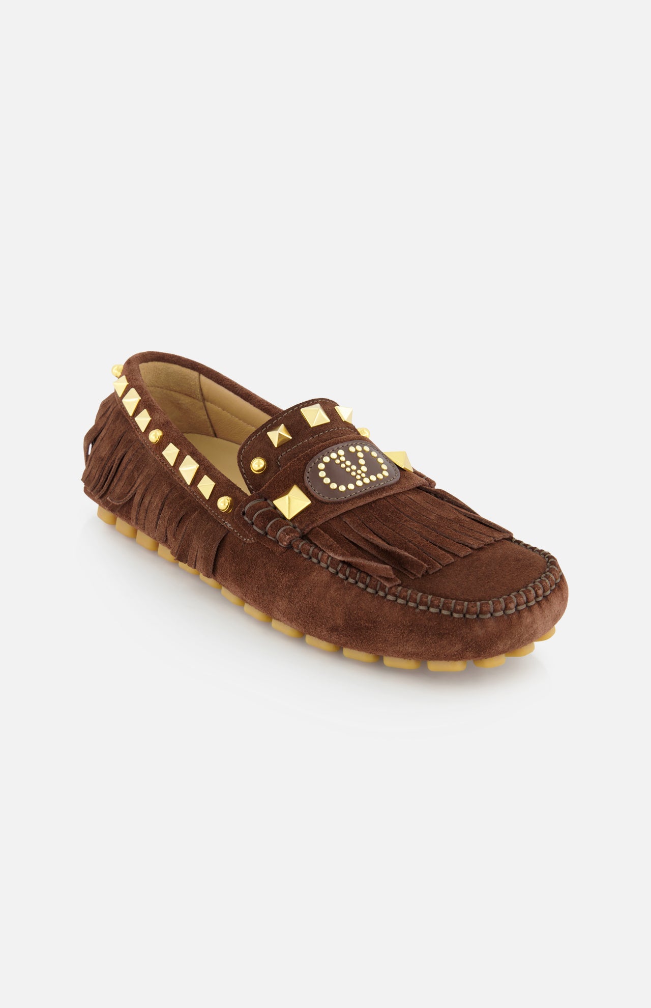 The VALENTINO GARAVANI VG Plaster Caster Driver Loafer T.05 is a handcrafted brown suede loafer with fringe trim, gold studs, detailed stitching, a rubber sole, and a studded circular design on the front flap.