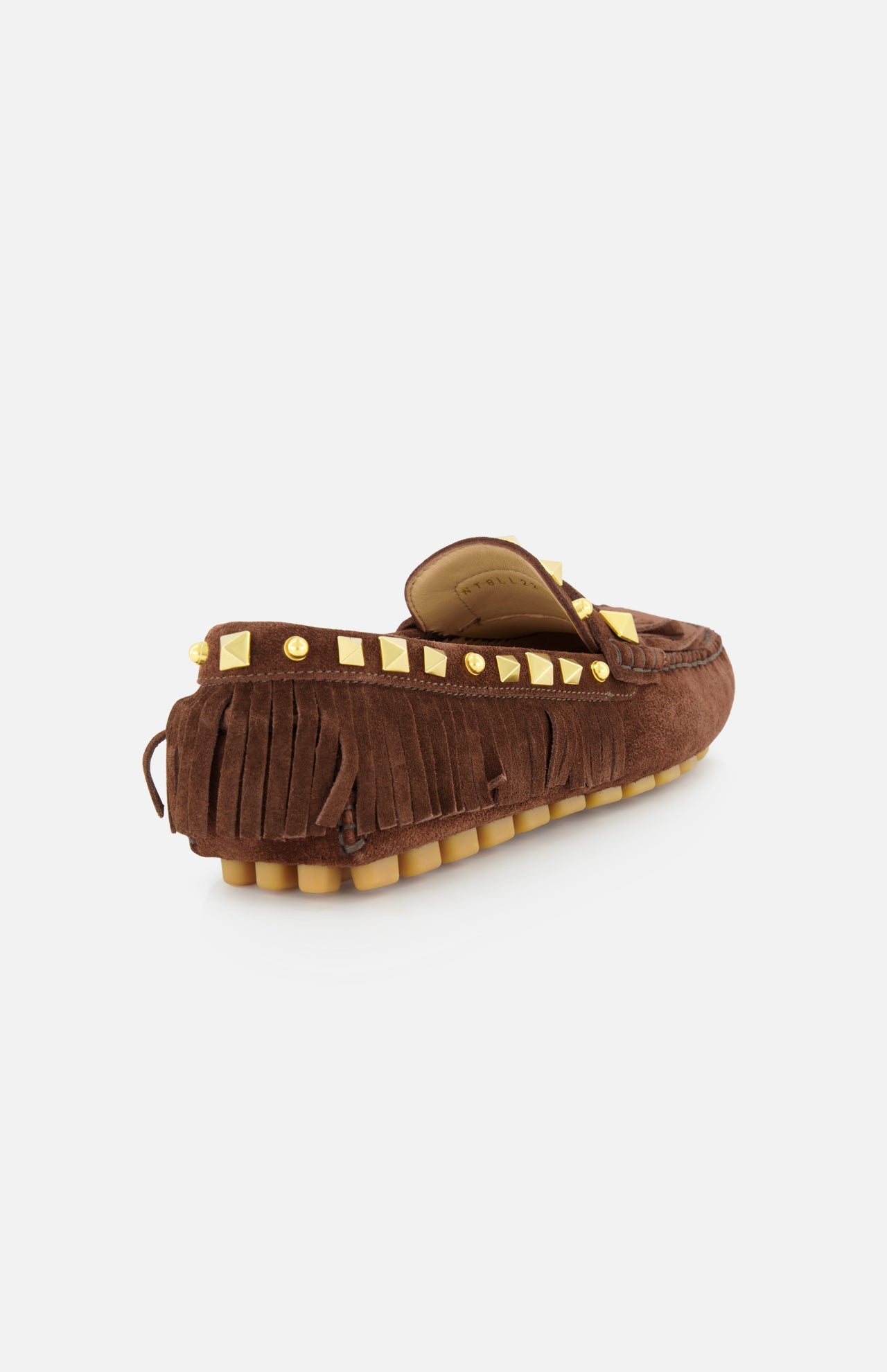 The VALENTINO GARAVANI VG Plaster Caster Driver Loafer T.05 is a brown suede bohemian loafer with handcrafted fringe trim, gold square studs on the heel collar, and a tan rubber sole with raised treads, shown angled from the back on white.