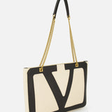 The VALENTINO GARAVANI Viva Superstar Medium Tote Bag features a rectangular cream leather design with a bold black VLogo on the front, gold chain straps, and black leather shoulder detail, shown against a white background.