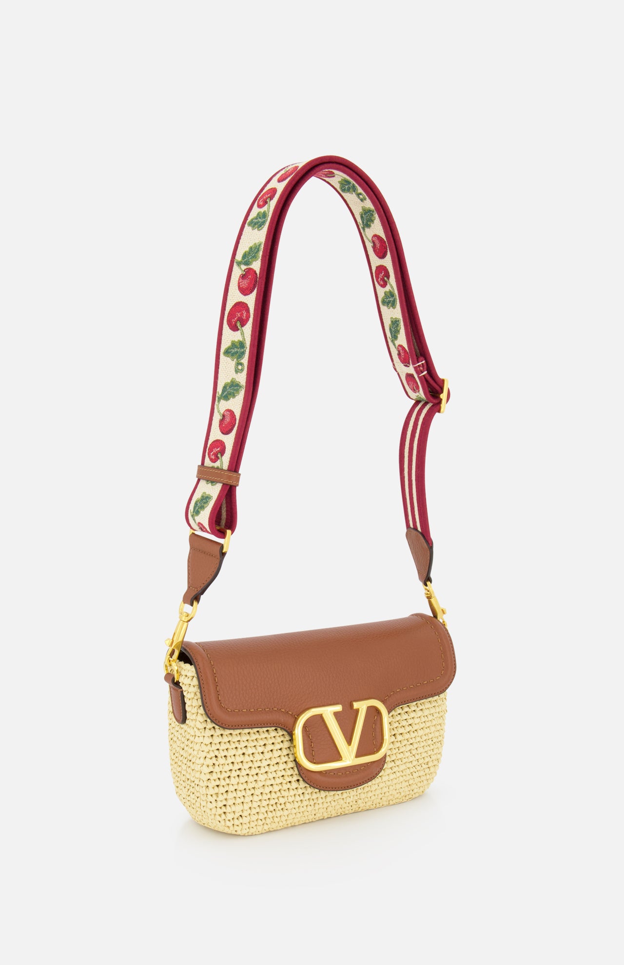The VALENTINO GARAVANI Alltime Cherry Strap Shoulder Bag features a woven straw base, brown leather flap with gold V logo, and a wide red strap embroidered with cherry motifs for a floral accent on this chic crossbody clutch.