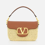 The VALENTINO GARAVANI Alltime Cherry Strap Shoulder Bag features a woven straw base, brown leather flap and handle, gold hardware, and a bold gold “V” logo on the front for stylish elegance.