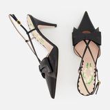 The VALENTINO GARAVANI Bowow Sling Back Heel is a pair of black leather pointed-toe pumps with large front bows, adjustable ankle straps, floral-patterned insoles, shown against a white background.