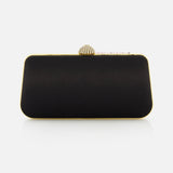 The VALENTINO GARAVANI Carry Secrets Miniaudiere Bag is a rectangular black clutch with gold edging and a decorative gold clasp, inspired by the elegance of Swarovski crystal clutches, set against a plain white background.