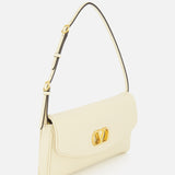 The Devain Small Shoulder Bag by VALENTINO GARAVANI is crafted from cream-colored lambskin leather and features an adjustable strap, gold VLOGO hardware, and a decorative logo clasp on the front flap, shown against a plain white background.