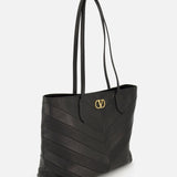 Valentino Garavani Jean Medium Tote Bag in black with chevron-stitched panels and a gold metal logo emblem on the front.