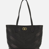 Valentino Garavani Jean Medium Tote Bag in black leather with a chevron-stitched pattern and a gold metal logo emblem at the top center.