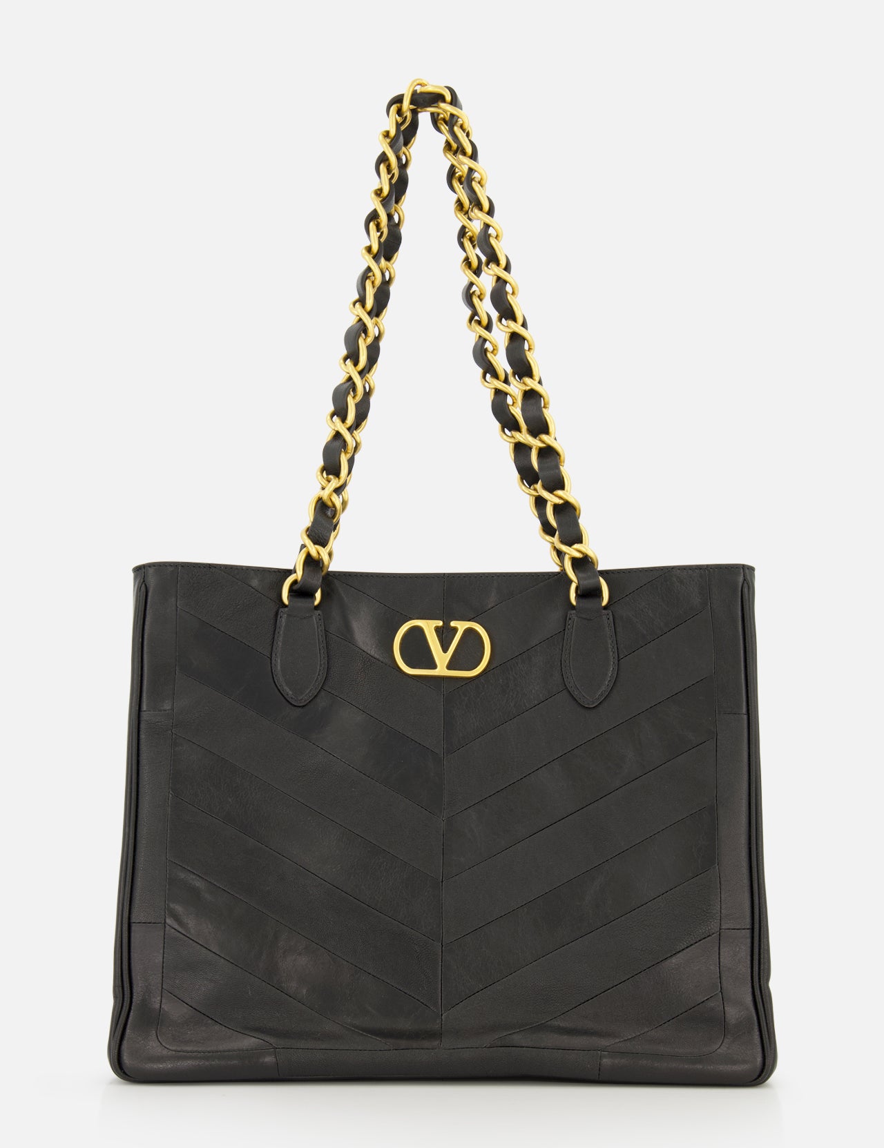 The VALENTINO GARAVANI Laseine Chevron Tote Bag, crafted from black leather, features a gold chain shoulder strap, a prominent gold V logo on the front, and an elegant chevron patchwork design, all showcased against a white background.