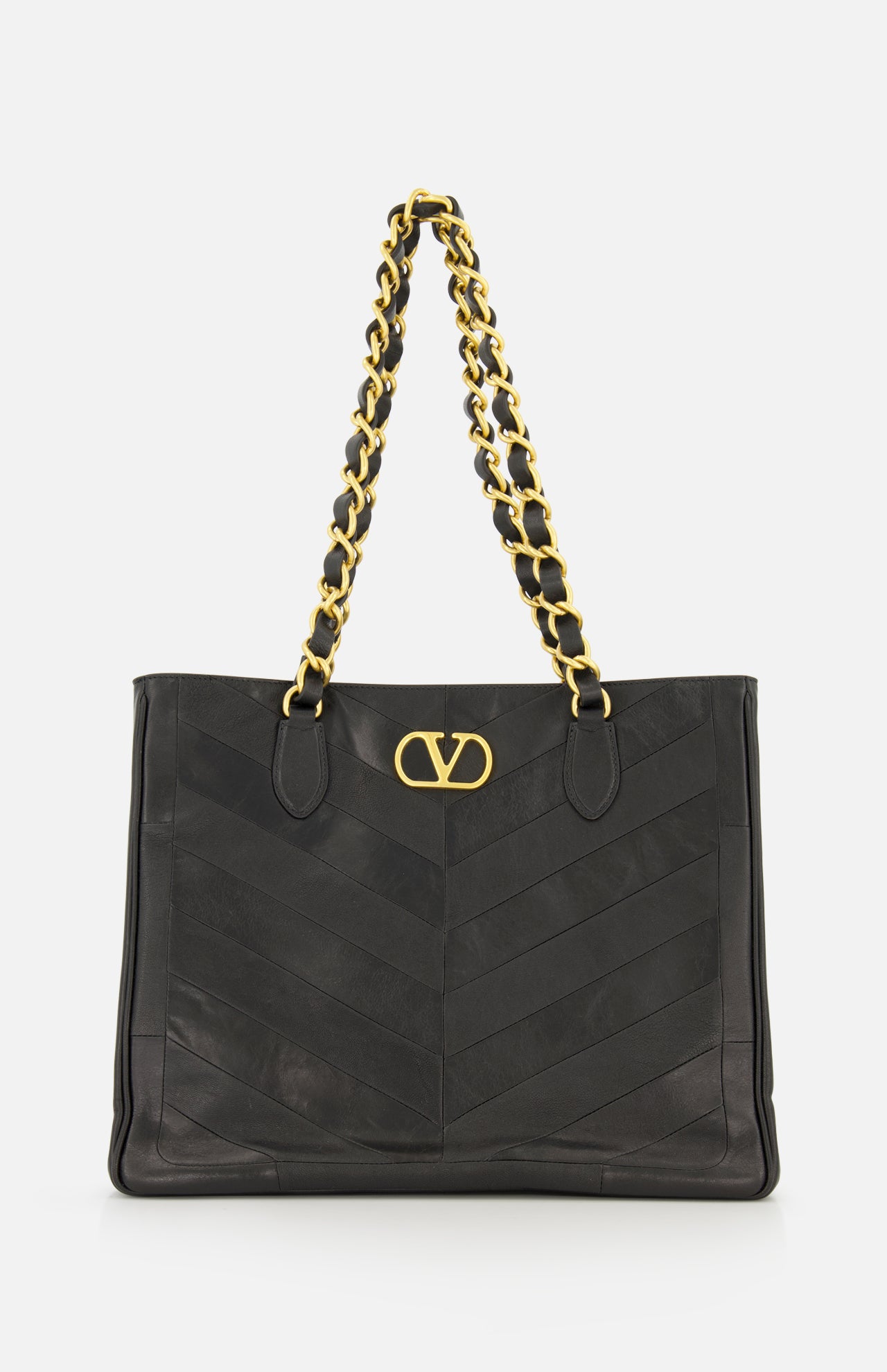The VALENTINO GARAVANI Laseine Chevron Tote Bag, crafted from black leather, features a gold chain shoulder strap, a prominent gold V logo on the front, and an elegant chevron patchwork design, all showcased against a white background.