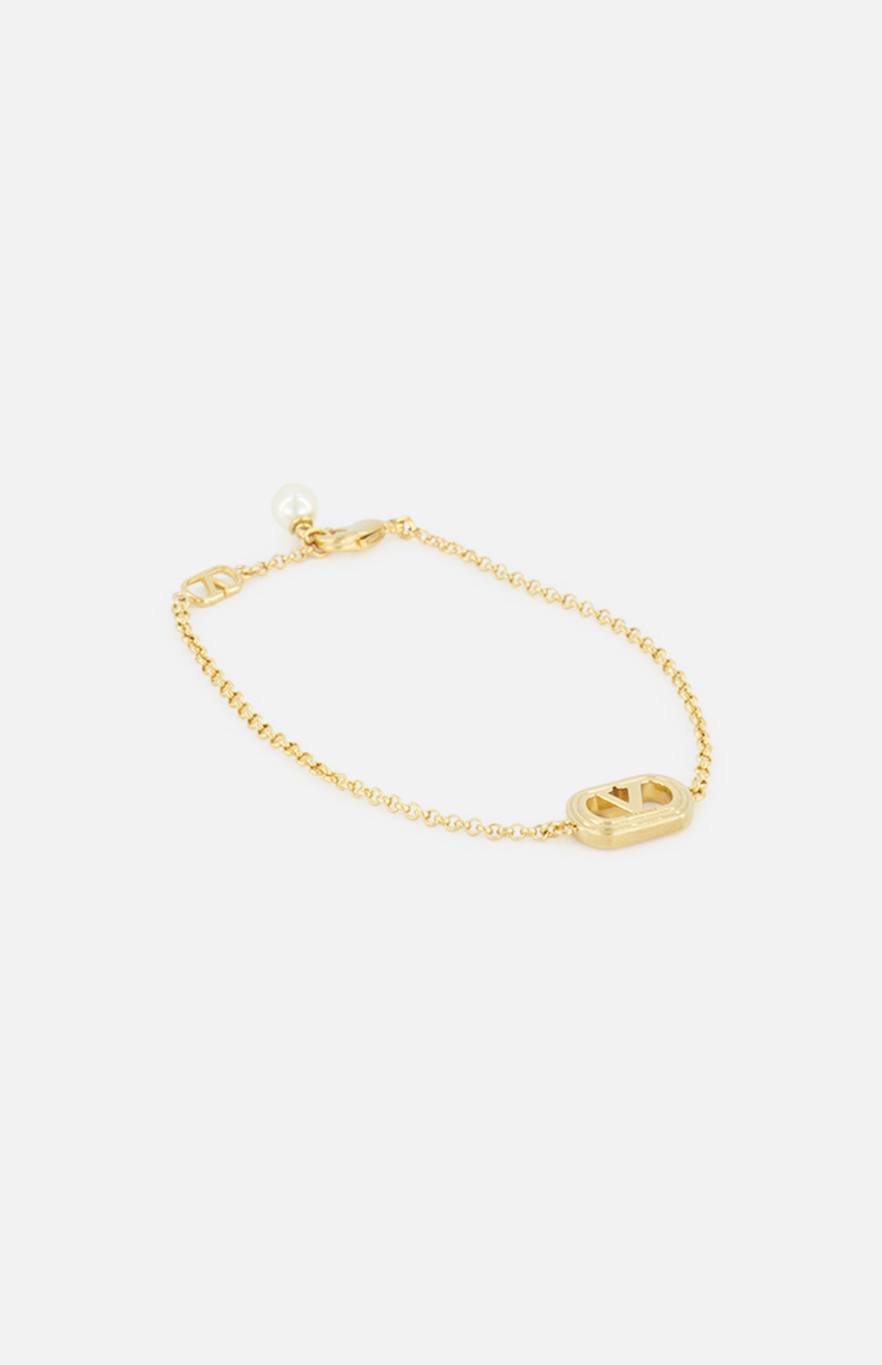 The VALENTINO GARAVANI Ovalette Pearl Bracelet features a delicate gold-tone chain, an oval cut-out charm with logo detailing, and a round Swarovski pearl accent by the clasp, shown on a white background.