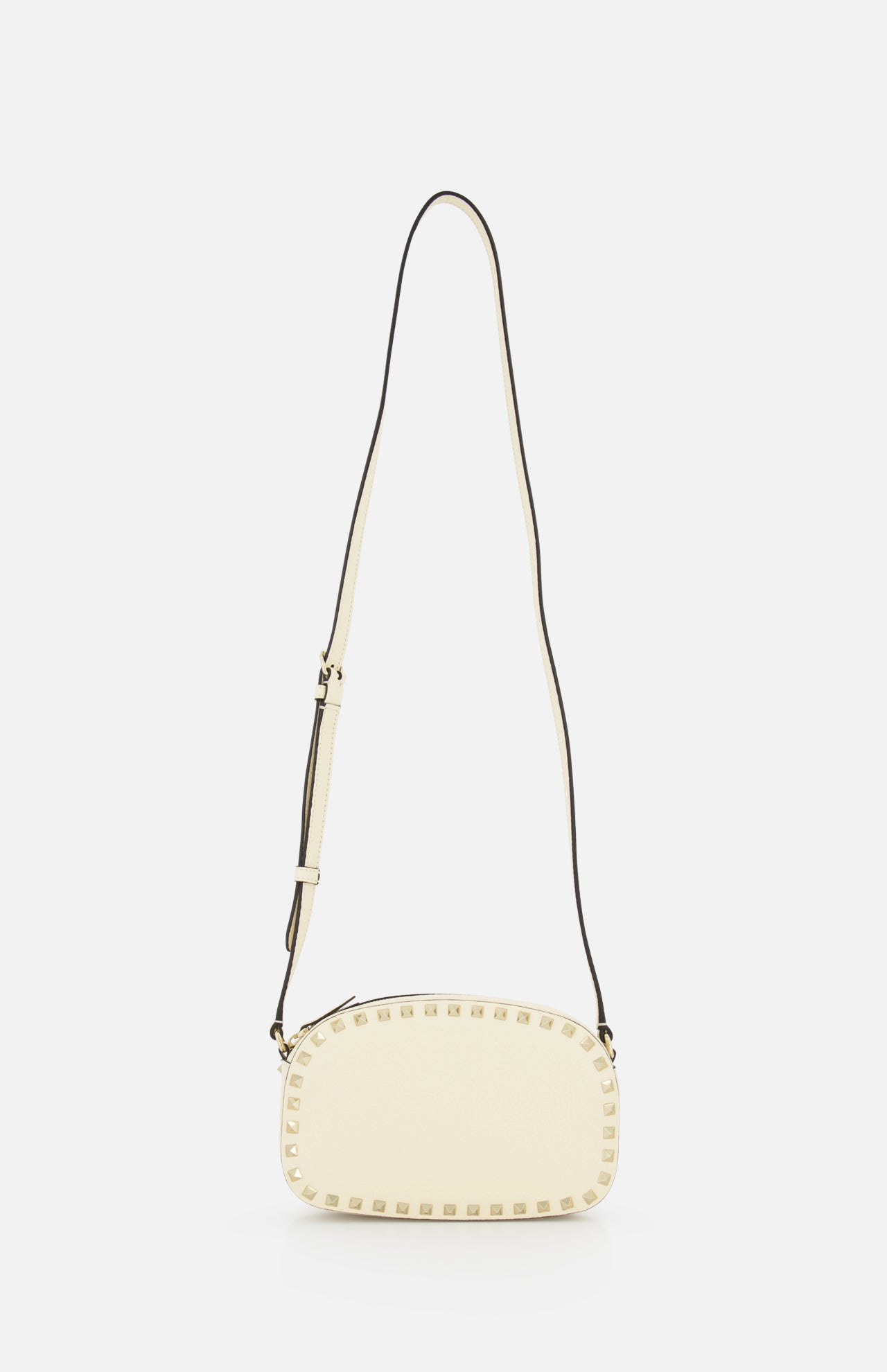 The VALENTINO GARAVANI Rockstud Camera Case Bag is a cream oval handbag with gold-tone studs along the edges and an adjustable long strap, shown against a plain white background.