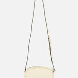 The VALENTINO GARAVANI Rockstud Camera Case Bag is an ivory leather crossbody in a cream hue, featuring gold-tone square studs along the edges and an adjustable dark strap, shown against a plain white background.