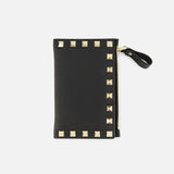 The VALENTINO GARAVANI Rockstud Coin Purse is a black leather card holder with a sleek zippered coin compartment, accented by gold pyramid rockstud trim along the edges and finished with a zipper featuring a black pull tab, shown against a white background.