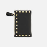 The VALENTINO GARAVANI Rockstud Coin Purse is a black leather pouch with a wrist strap and elegant gold square rockstud trim along two edges. It features a zippered coin compartment and is shown against a plain white background.