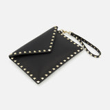 The VALENTINO GARAVANI Rockstud Medium Flat Pouch is a black envelope clutch crafted in textured leather, adorned with gold pyramid rockstuds along the edges and featuring a matching studded wrist strap, displayed on a white background.