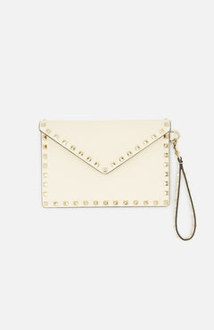 The VALENTINO GARAVANI Rockstud Medium Flat Pouch is an ivory clutch with a classic envelope design, embellished with gold rockstuds along the edges and featuring a detachable wrist strap, displayed against a plain white background.