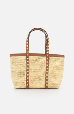 The VALENTINO GARAVANI Rockstud Mini Tote Bag is crafted from woven raffia and leather with brown handles, gold rockstud accents, and an open-top rectangular design for easy access.