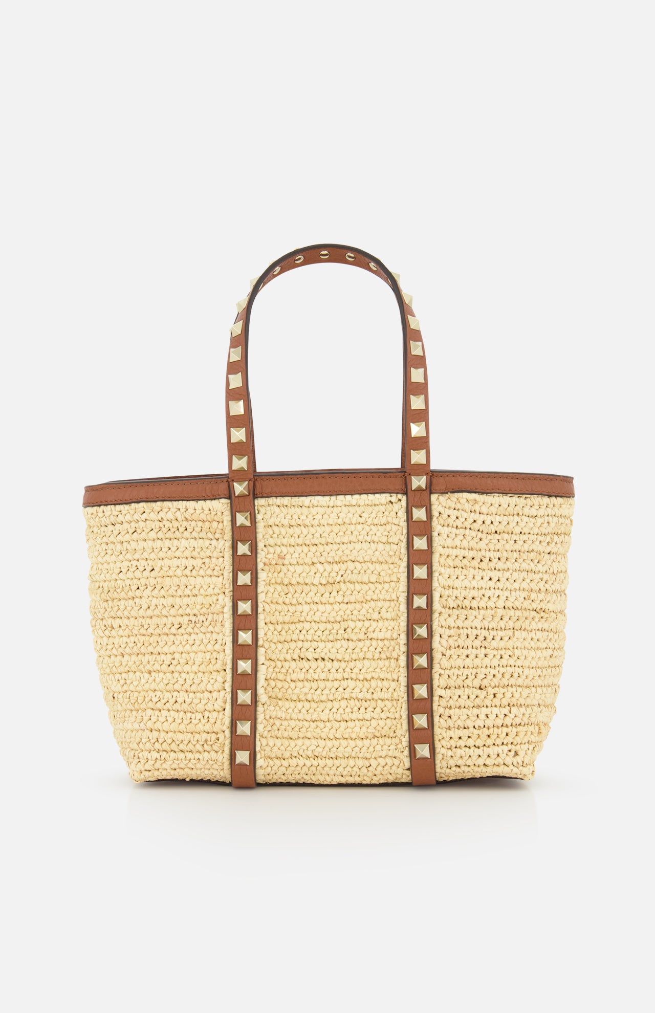 The VALENTINO GARAVANI Rockstud Mini Tote Bag features woven raffia and leather with brown handles and gold rockstud accents. This rectangular, open-top bag is shown against a plain white background.
