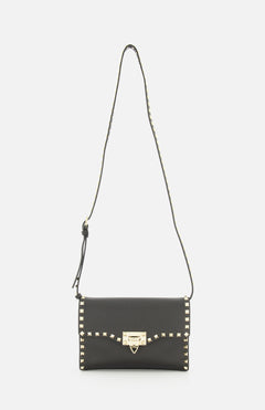 The VALENTINO GARAVANI Rockstud Small Shoulder Bag is crafted from black Italian leather and features gold square studs along the edges, a gold buckle closure at the front, and an adjustable studded strap—an effortlessly chic handbag.