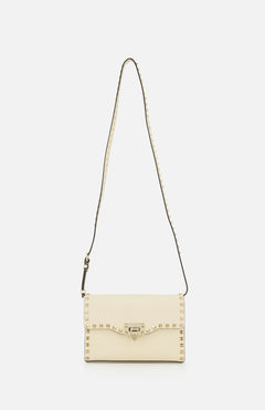 Introducing the Rockstud Small Shoulder Bag by VALENTINO GARAVANI, a refined cream-colored rectangular accessory crafted in elegant ivory. This sophisticated handbag is detailed with signature gold pyramid studs outlining its flap closure and extends to the adjustable studded strap, elevating its modern appeal. Shot against a plain white background, this versatile piece seamlessly combines chic styling with timeless charm.