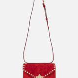 The VALENTINO GARAVANI Rockstud Small Suede Shoulder Bag in lipstick red features gold-tone rockstud trim, a gold clasp, and an adjustable brown leather strap, shown on a plain white background.
