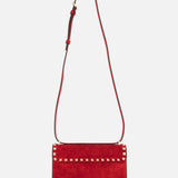 The VALENTINO GARAVANI Rockstud Small Suede Shoulder Bag in lipstick red features rockstud trim on the top flap and an adjustable matching strap, displayed against a plain white background.