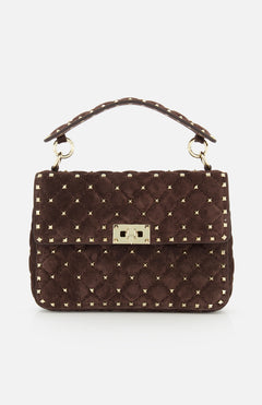 The VALENTINO GARAVANI Rockstud Spike Medium Shoulder Bag features dark brown quilted suede adorned with signature gold micro rockstuds, a top handle, and a gold rectangular clasp on the front flap.