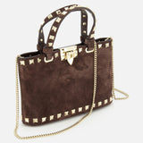 The VALENTINO GARAVANI Rockstud Suede Mini Bag is crafted from dark chocolate brown suede and embellished with gold pyramid studs. It features a top handle, a removable chain strap, and a gold hardware clasp, shown here against a white background.