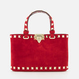 The VALENTINO GARAVANI Rockstud Suede Mini Bag features red suede, gold pyramid studs, dual handles, a detachable chain strap, and a gold clasp closure, shown against a plain white background.