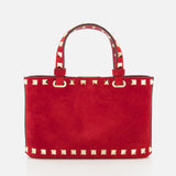 The VALENTINO GARAVANI Rockstud Suede Mini Bag with Chain Strap features gold pyramid studs along the red suede edges and handles, displayed against a white background.