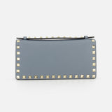 The VALENTINO GARAVANI Rockstud Wallet with Chain Strap is a rectangular, light blue leather crossbody bag featuring gold pyramid studs along the edges, perfect as a chic party purse and displayed against a plain white background.