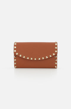The VALENTINO GARAVANI Rockstud Wallet with Chain Strap is a brown leather mini bag with a wallet-inspired shape, flap closure, and gold rockstud trim along the edges, shown on a plain white background.