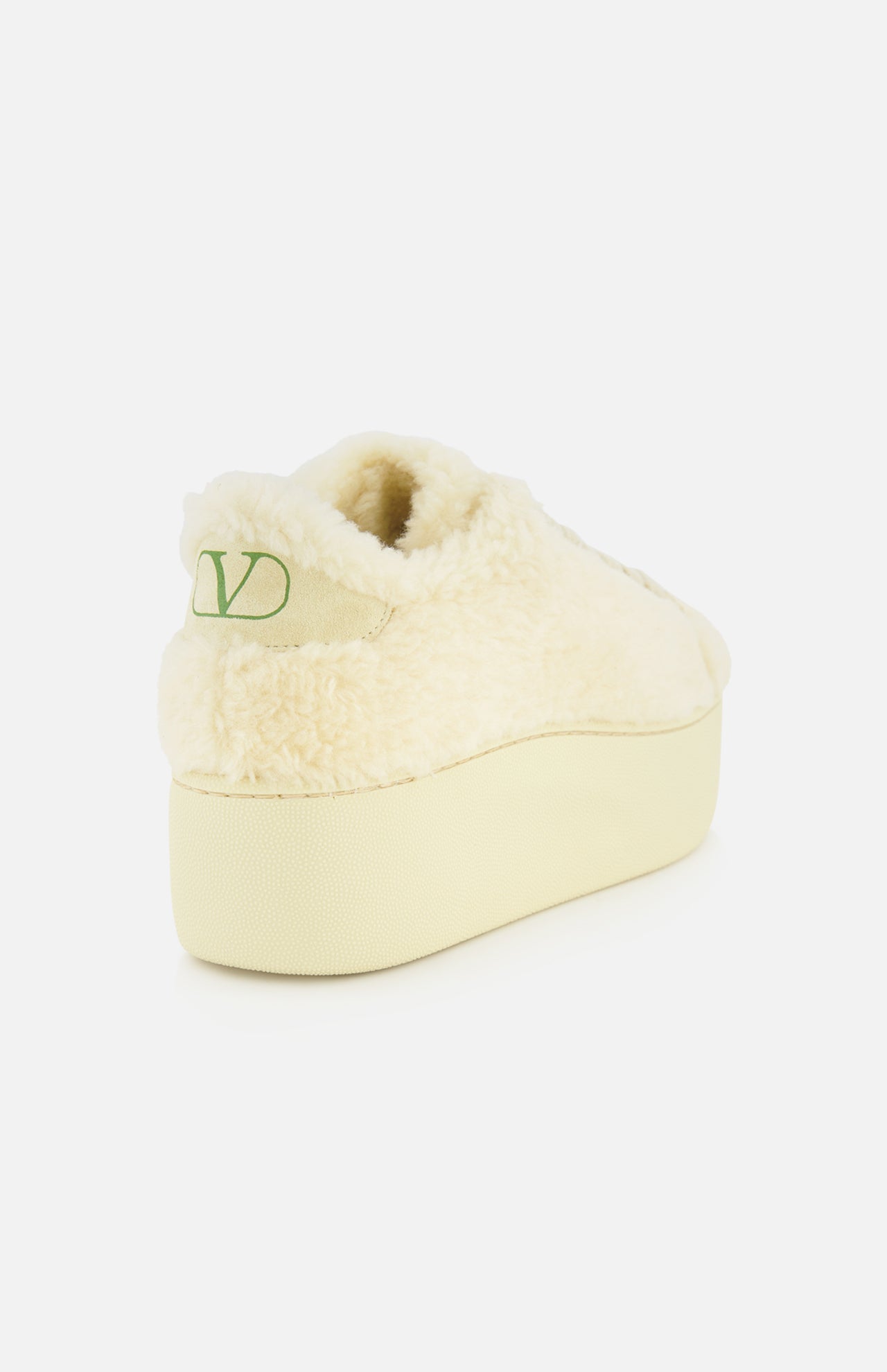The VALENTINO GARAVANI Royco Shearling Platform Sneaker is shown from the back, highlighting its cream-colored shearling construction and thick platform heel. A green V-shaped logo detail appears on the left side of the heel.