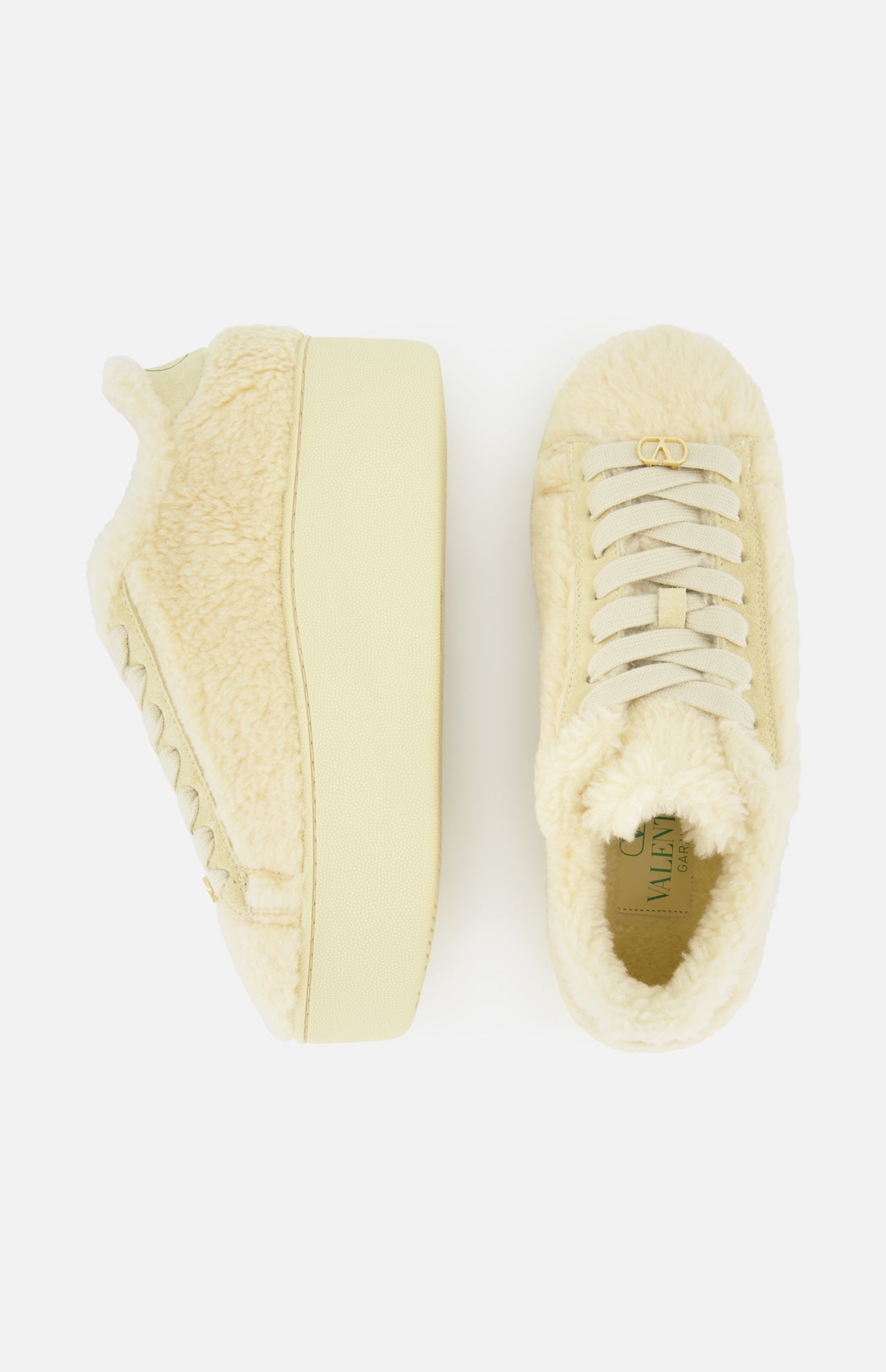 The VALENTINO GARAVANI Royco Shearling Platform Sneaker is pictured in a pair, each showcased from the side and top view. The sneakers feature cream-colored, soft shearling uppers with light-toned laces and thick platform soles. Subtle logo detailing accents the design, all set against a white background.