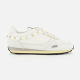 Valentino Garavani Stud Up Sneaker in white, featuring a low-top silhouette, a horizontal strap across the heel with gold rockstud trims, and a layered rubber sole.