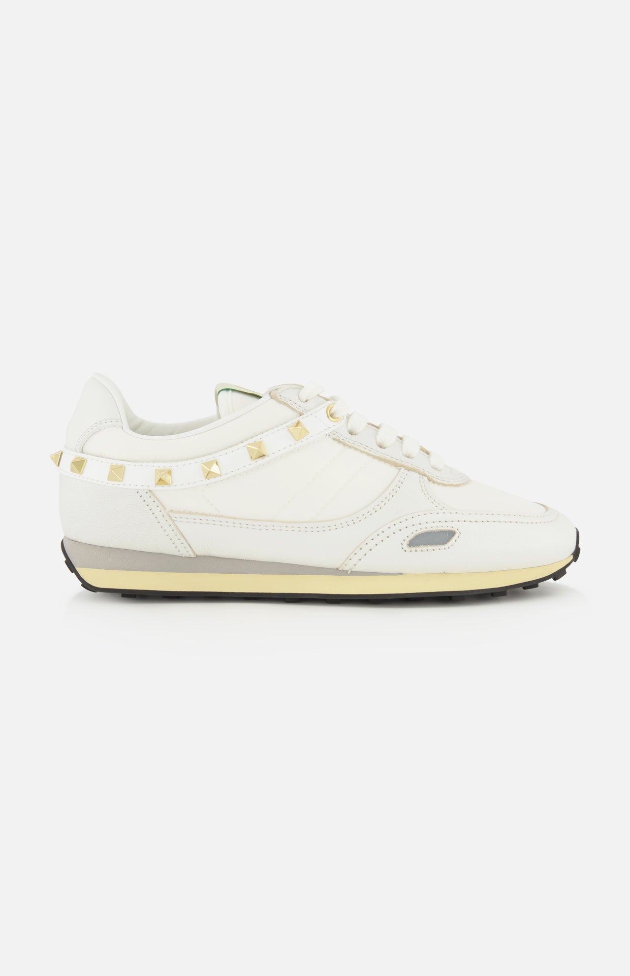 Valentino Garavani Stud Up Sneaker in white, featuring a low-top silhouette, a horizontal strap across the heel with gold rockstud trims, and a layered rubber sole.