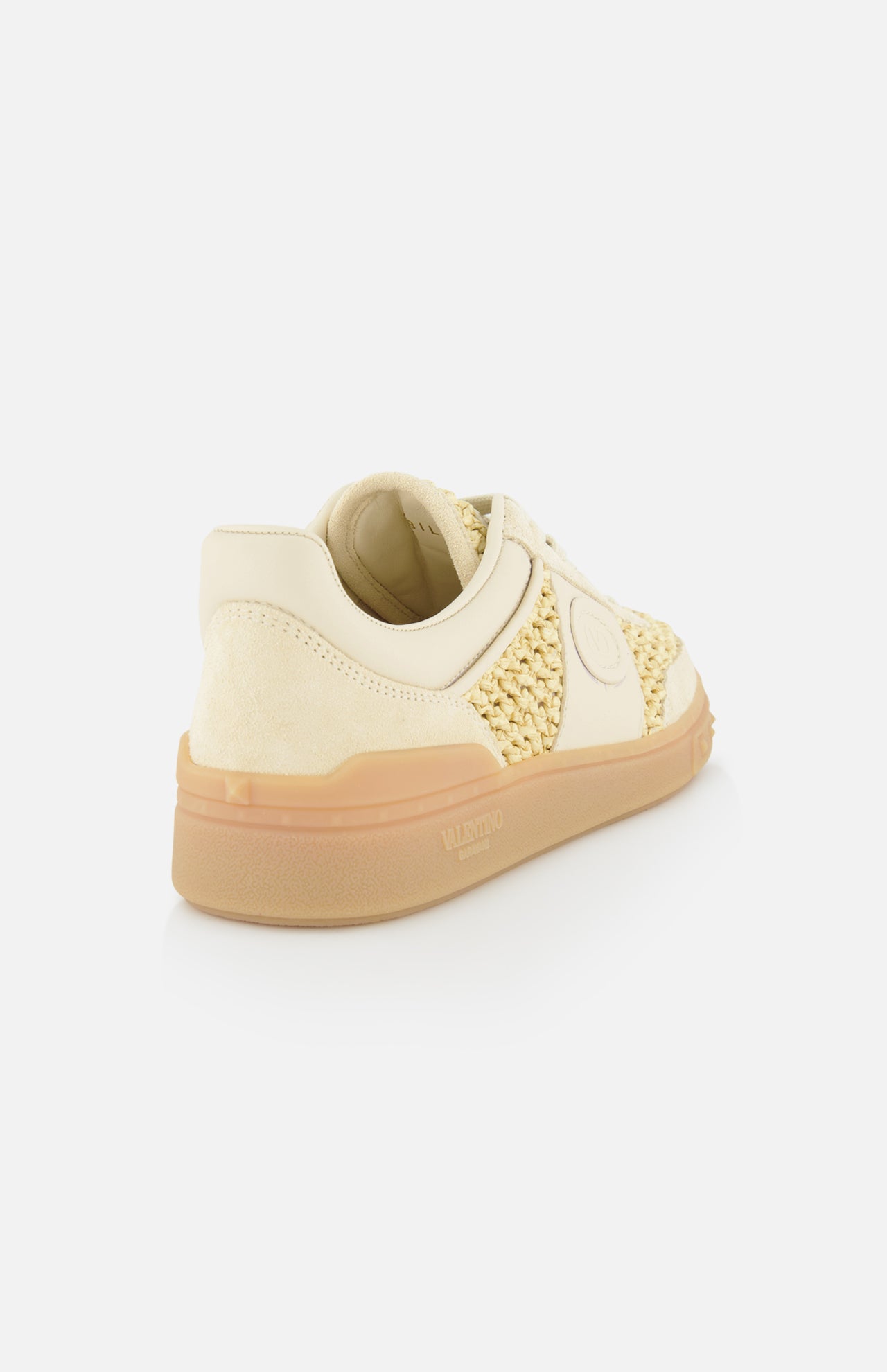 The VALENTINO GARAVANI Upvillage Raffia Sneaker features cream and beige hues, woven raffia side panels, a suede heel, rubber sole, and an embossed Valentino logo on the heel—shown angled to display the side and back on a white background.