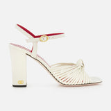 The Valentino Garavani Annet T.90 Sandal by VALENTINO GARAVANI features white knotted leather straps, a leather ankle strap with gold buckle, an ivory high heel, and a subtle VLogo accent near the sole.